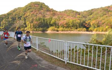 紅葉が見頃のダム湖沿いを走る選手たち=御前山ダム