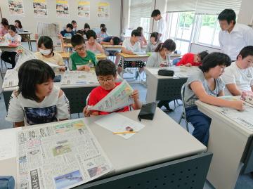 当日の茨城新聞を手にする児童たち=古河市立仁連小