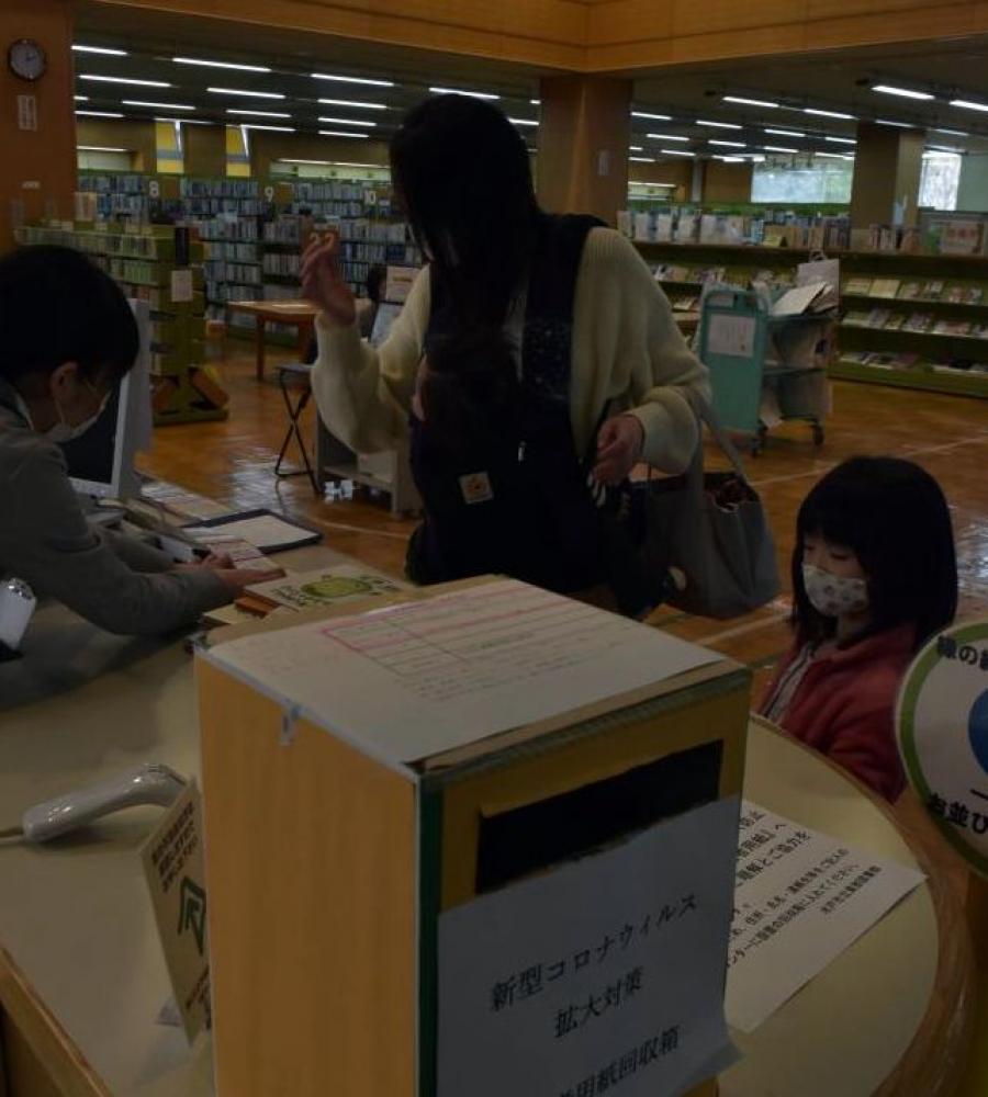 約1カ月ぶりに開館した水戸市立東部図書館で、予約していた絵本を借りる親子=同市元吉田町