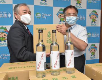 筑西市の須藤茂市長に、アルコール度数70%の自社製消毒液を手渡す来福酒造の藤村俊文社長(右)=筑西市役所