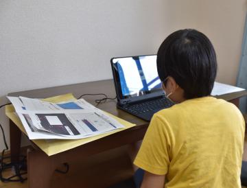 自宅でタブレット端末を立ち上げる男子児童