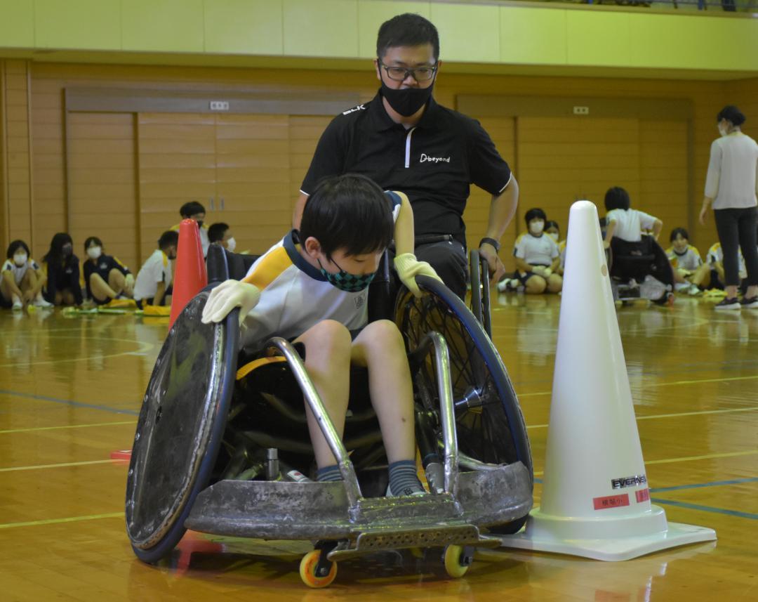 競技用車いすに挑戦する児童を見守る三阪洋行さん=那珂市横堀の市立横堀小