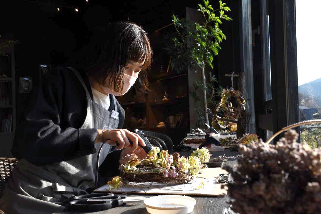 グルーガンでドライフラワーをリース台に付けていく潮田宏美さん=石岡市下青柳のいばらきフラワーパーク