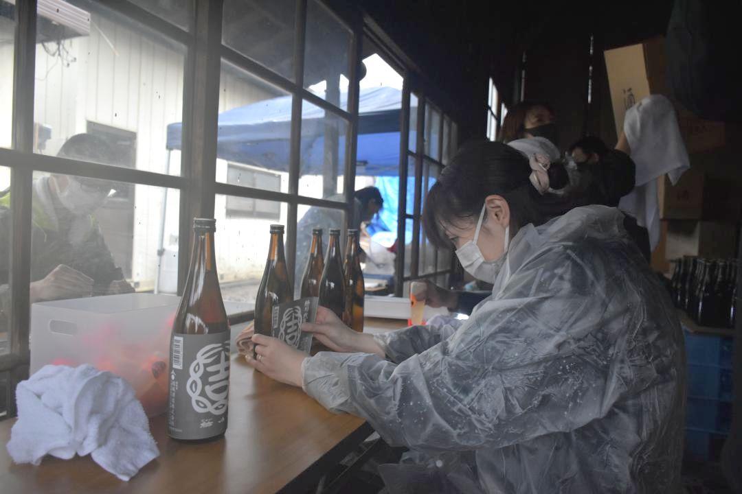 結城酒造の焼け残った作業場で日本酒の瓶にラベルを貼り付けるスタッフ=結城市結城
