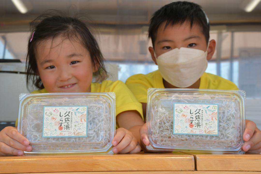 自分たちがパッケージをデザインしたシラスの商品を持つ子どもたち=高萩市本町