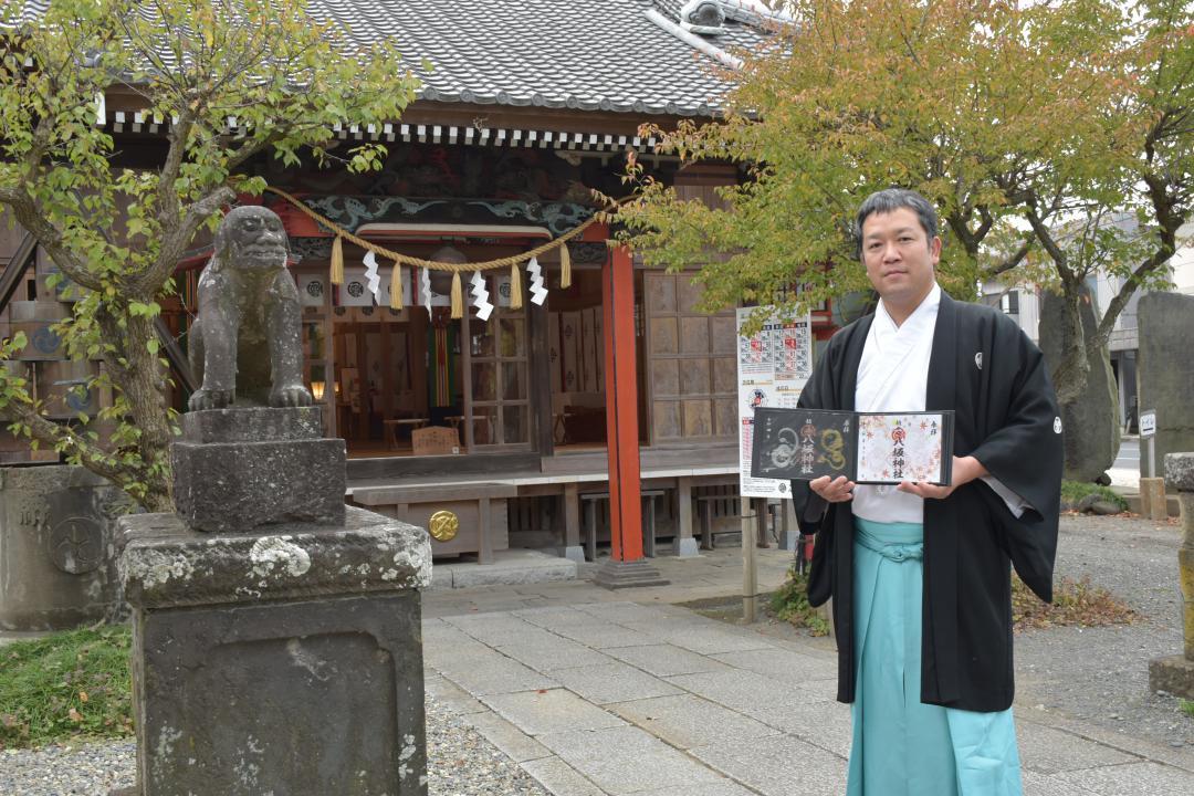 拝殿の前で、通年と月替わりの御朱印を持つ宮司の和歌森将城さん=龍ケ崎市上町
