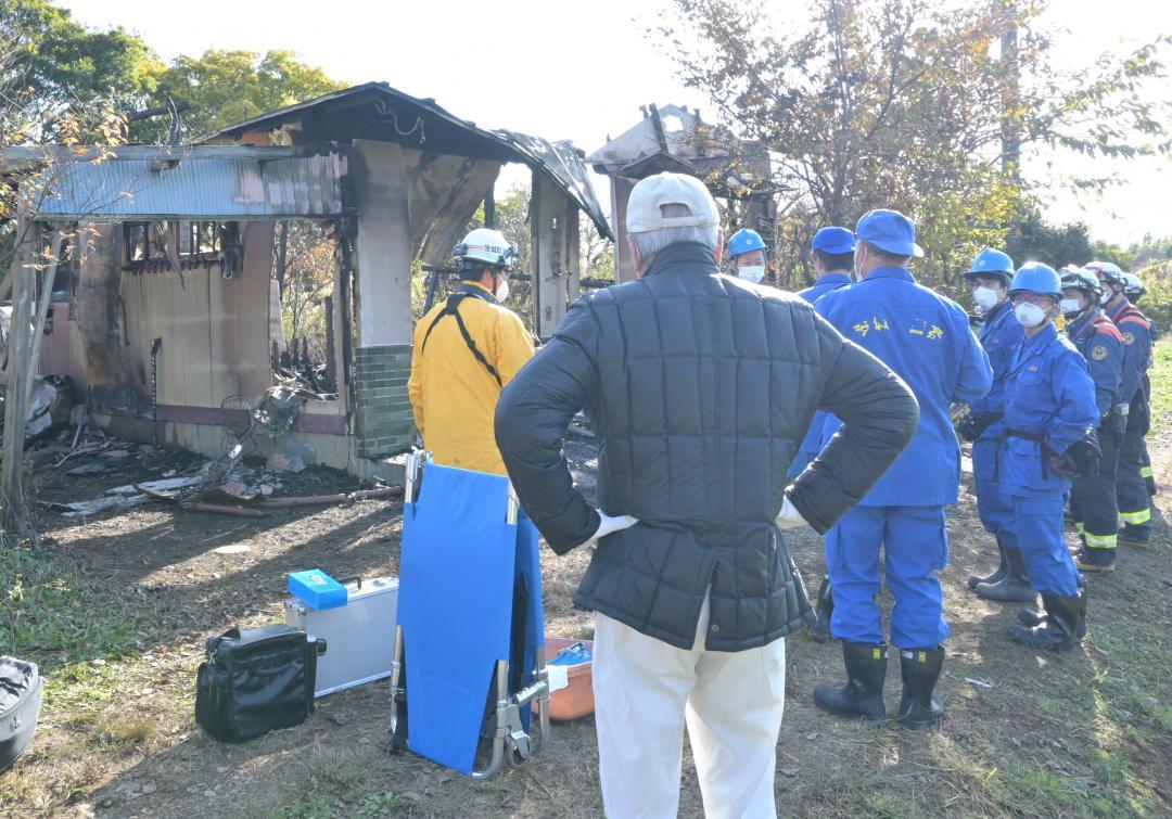 火災発生翌日に焼け跡を見つめる海老沢正夫さん(中央手前)=11月17日午前、茨城町下石崎
