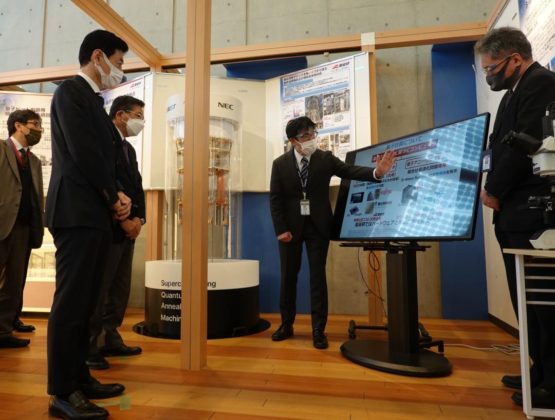産総研の職員から量子研究開発の説明を受ける西村康稔経産相(手前左)=つくば市梅園