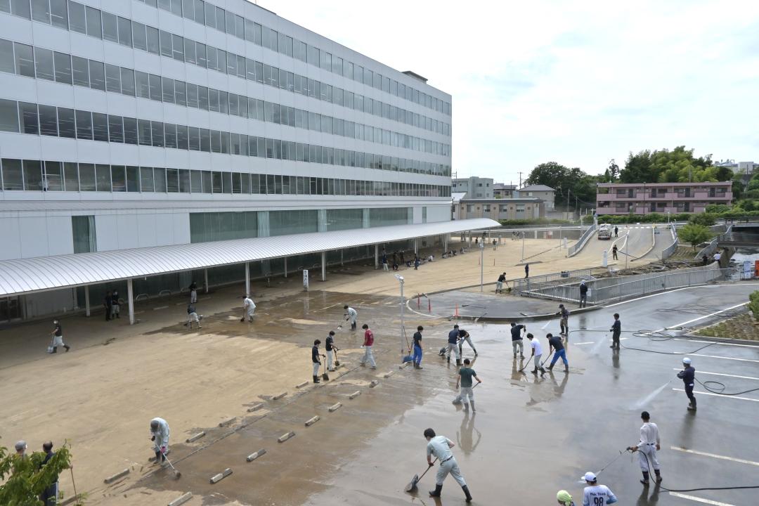 数沢川(中央右)の氾濫で汚れた駐車場を清掃する市職員=11日午前10時半ごろ、日立市役所