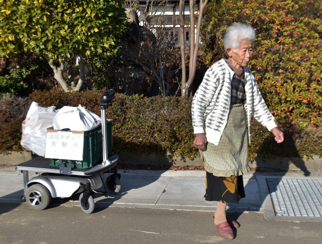 白石みとりさんの後ろに付いて荷物を運ぶ自動追従ロボット=つくば市小田