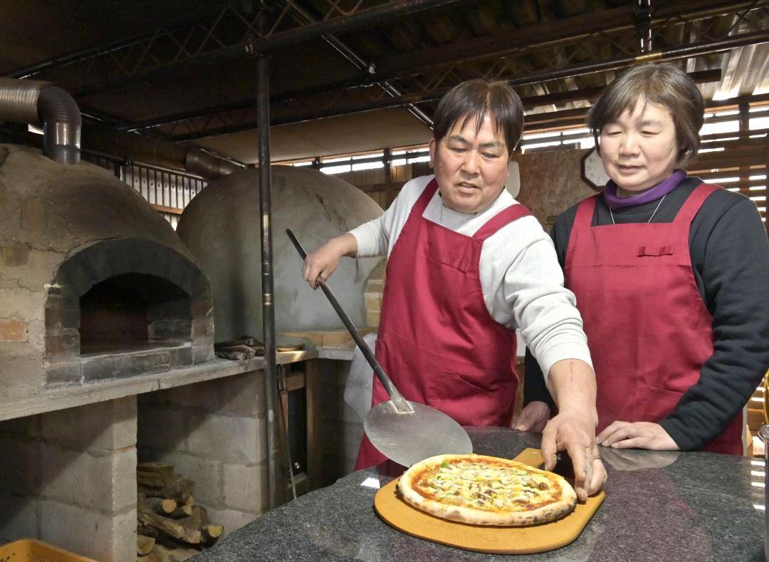 まき窯でピザを焼き上げる「マガリヤマ旨味工房」店主の曲山渉さん(左)。妻の幸枝さんと2人で店を営む=行方市小貫
