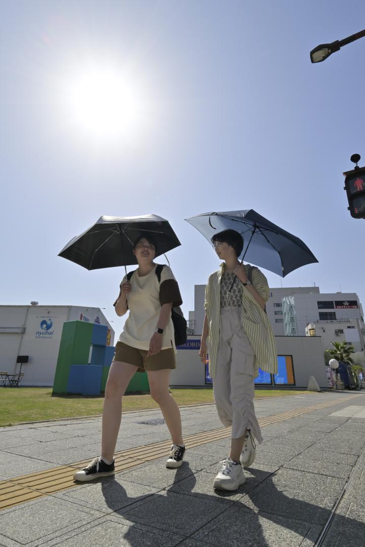 気温が上昇し日差しが降り注ぐ中、日傘を差して歩く人たち=4日午後2時29分、水戸市南町