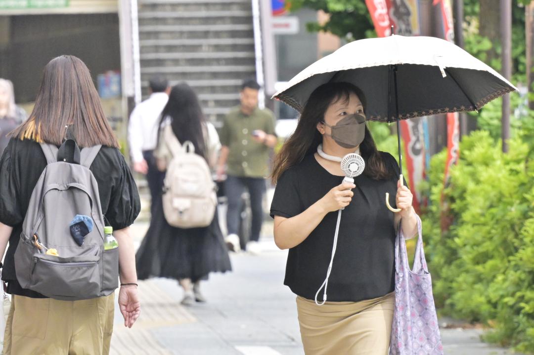 気温が上昇し、日傘と小型扇風機を手に歩く女性=同日午後3時21分、水戸市三の丸