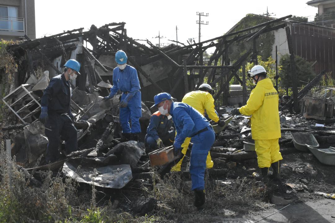 住宅が全焼した火災現場を調べる日立署員ら=日立市