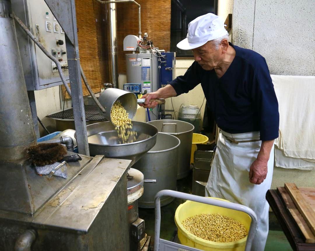 豆腐を作るため機械に輸入大豆を入れる倉田食品の倉田伸社長=下妻市原
