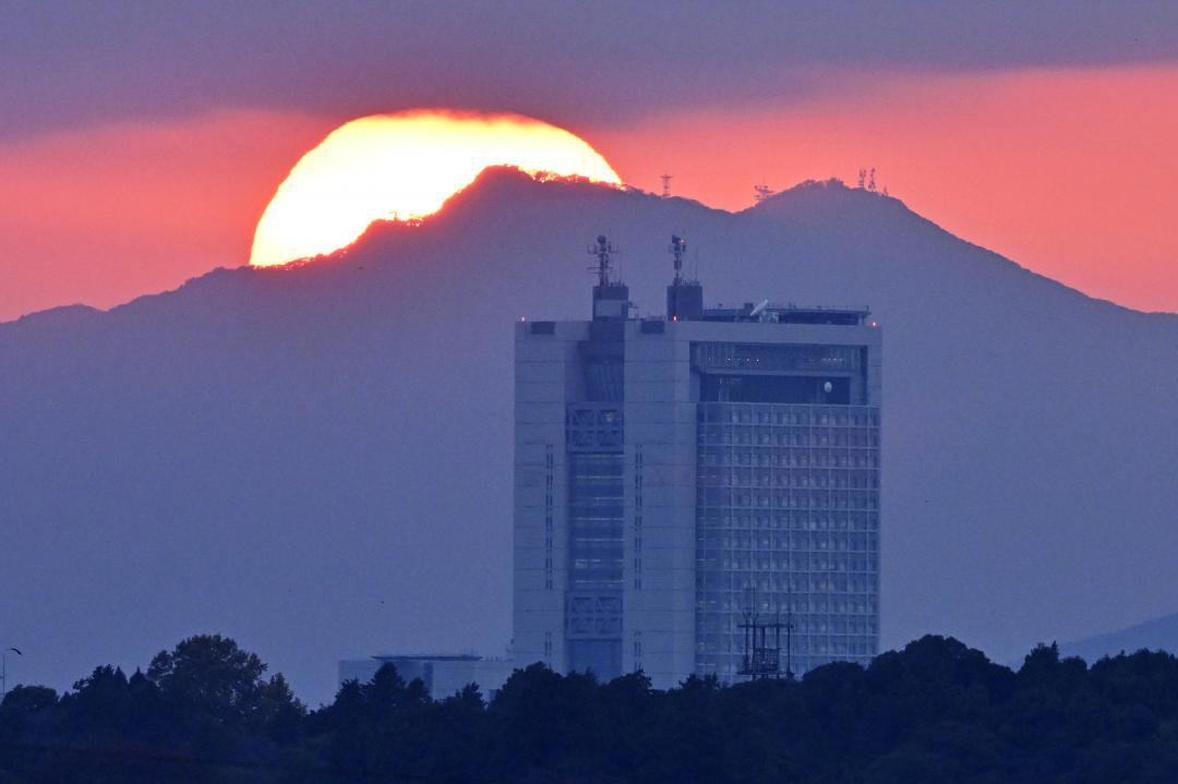 県庁の奥にそびえる筑波山頂付近に沈む夕日=12日午後4時24分、ひたちなか市金上
