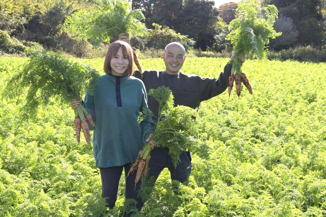 自慢のニンジンを手に笑顔を見せる大和田昌幸さんと妻のかおりさん=行方市中根
