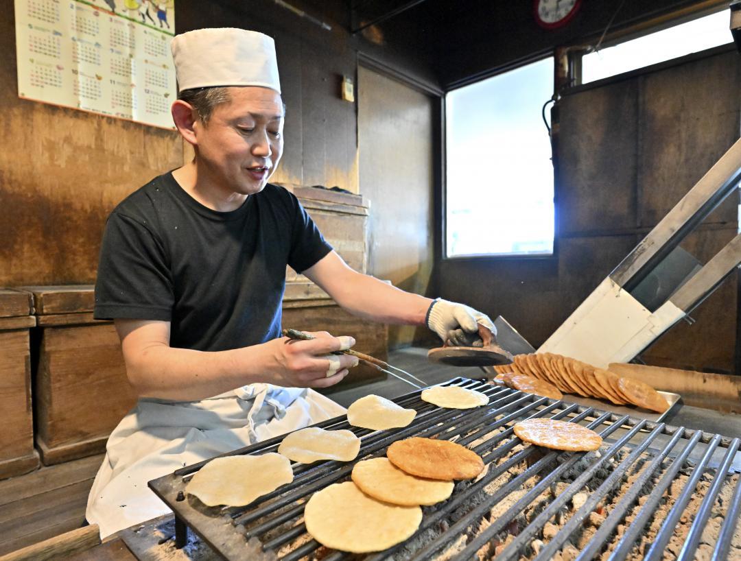 炭火でせんべいを焼く天野屋代表の鈴木義人さん、左手にはせんべいを平らに押さえるこて=常総市水海道宝町
