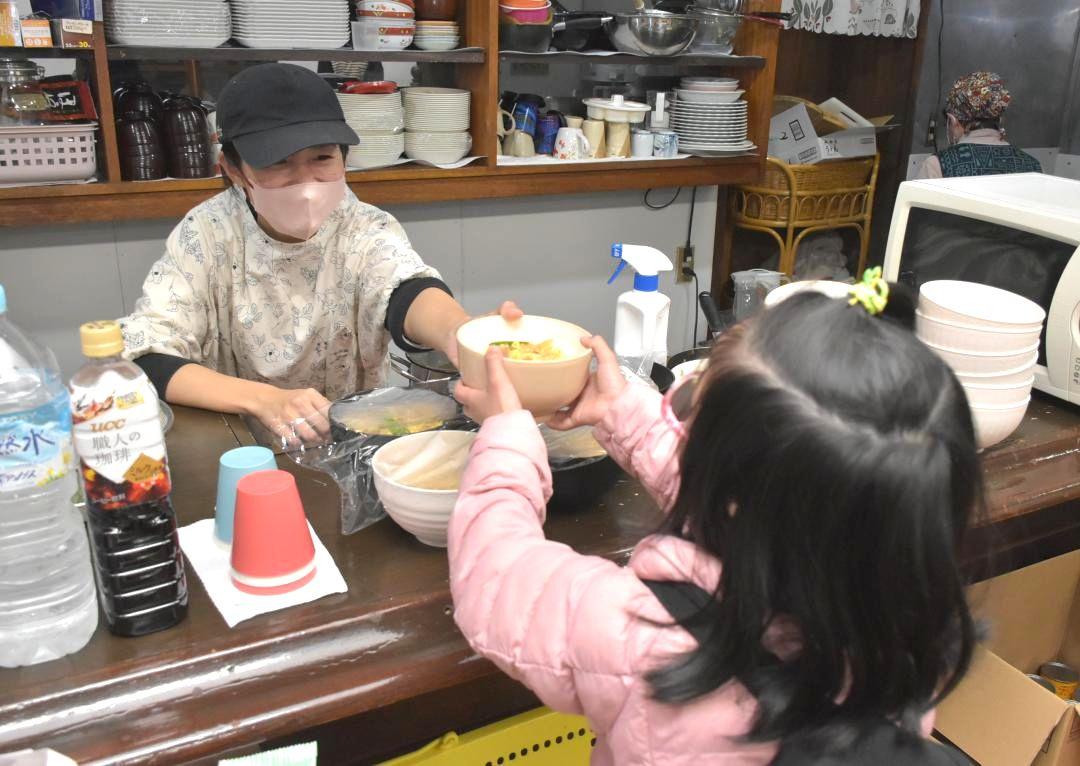 子ども食堂で親子丼を手渡す代表の堅野里桜さん(左)=1月20日、水戸市本町
