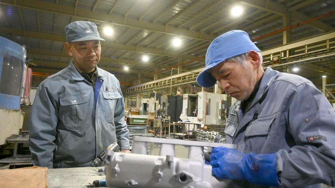 自動車部品の仕上げ作業を見つめる飯村精機製作所の飯村智社長(左)=土浦市本郷
