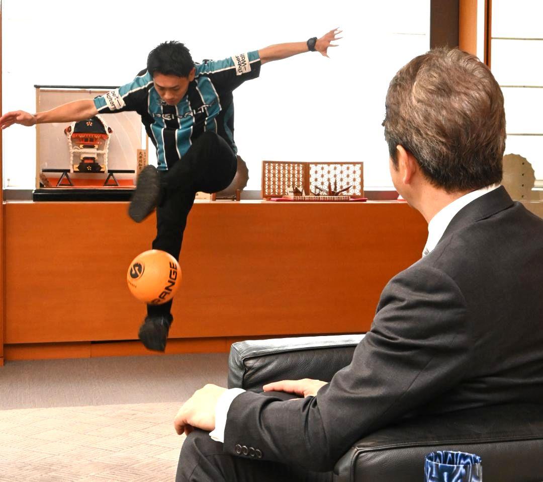 大井川和彦知事(右)にフリースタイルフットボールの技を披露するトミーさん=県庁
