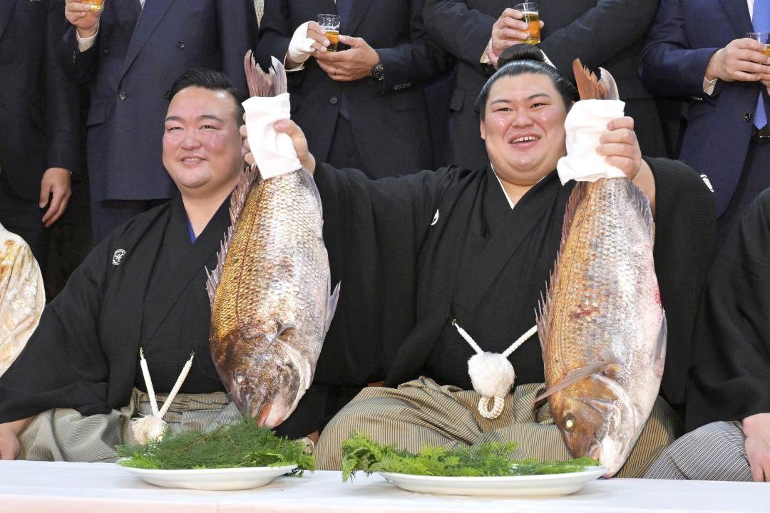 横綱昇進の伝達式後、タイを手に笑顔を見せる大の里(右)。左は二所ノ関親方=28日午前、阿見町荒川本郷の二所ノ関部屋