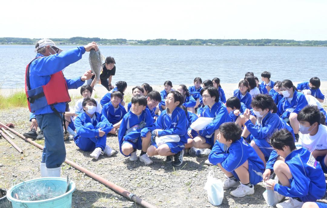 涸沼で水揚げされた魚を手に生徒に解説する清水勝利さん(左)=茨城町下石崎
