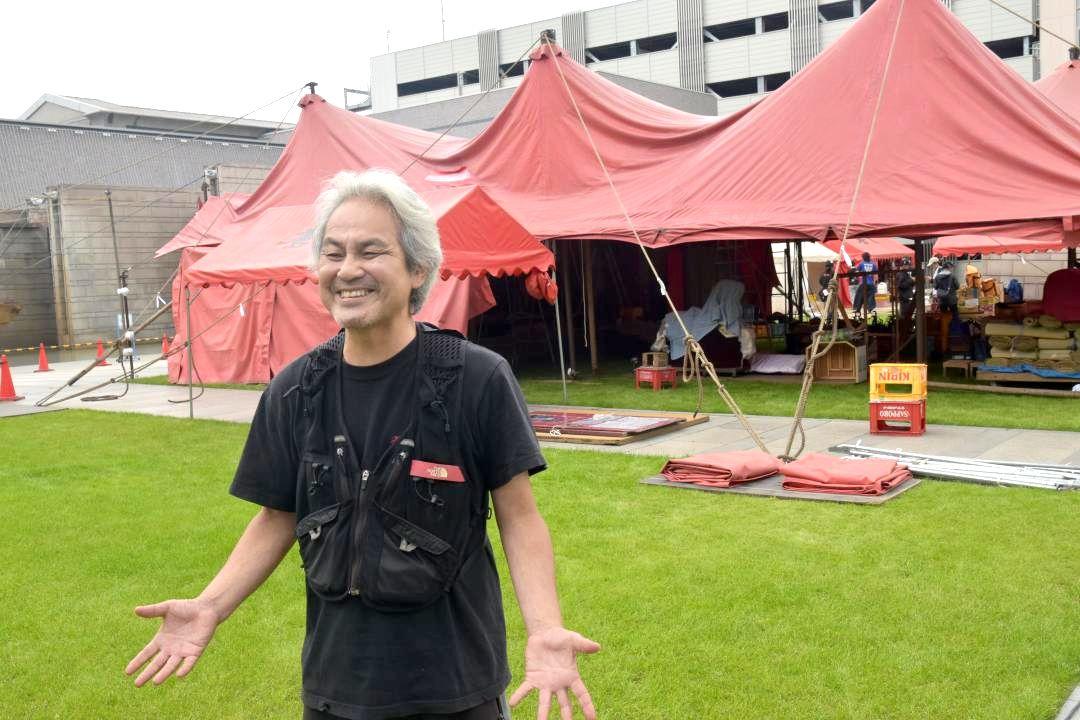 13年ぶりに水戸に設営された紅テントを前に取材に応じる久保井研さん=水戸市五軒町の水戸芸術館広場