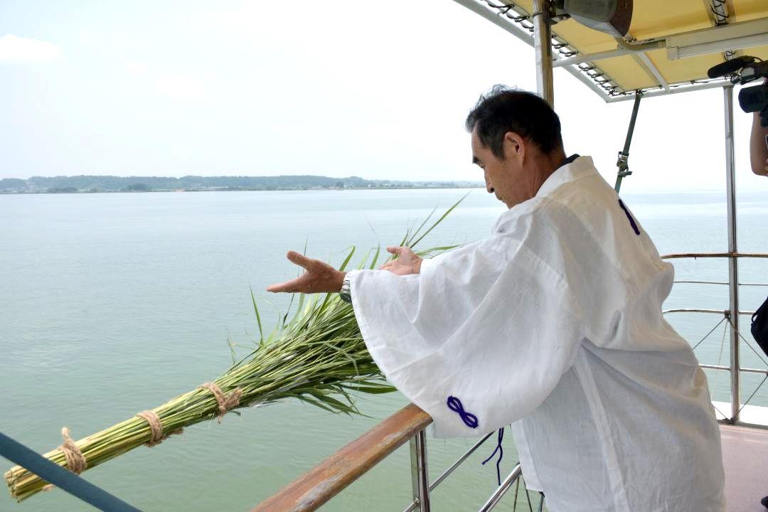形代の灰を包んだヨシの束を湖面に流す地区の代表者=土浦市沖の霞ケ浦
