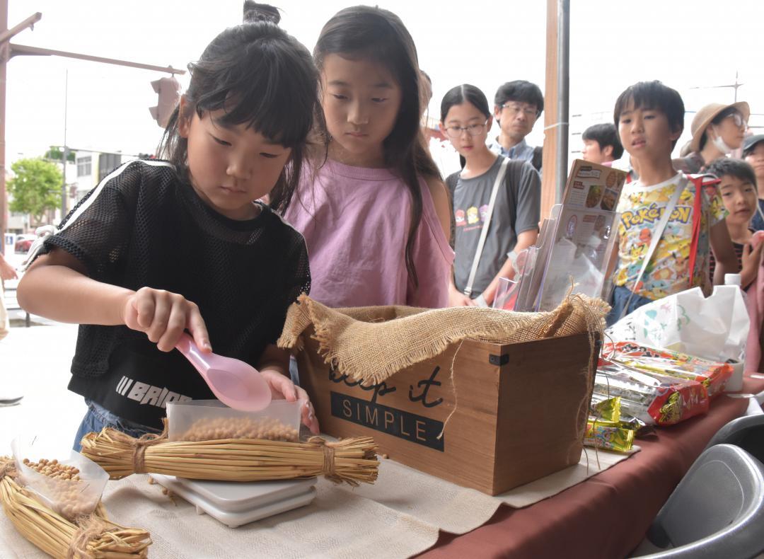 「水戸の納豆納涼祭」でわら納豆70グラムの重さ当てゲームに挑戦する子ども=水戸市泉町