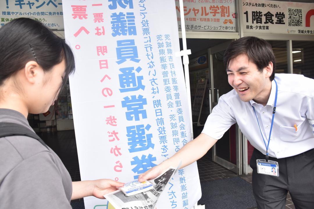 茨城大生に参院選の投票日やキャンパス内に開設された期日前投票所を伝えるチラシを配る県選挙管理委員会の担当者(右)=15日、水戸市文京
