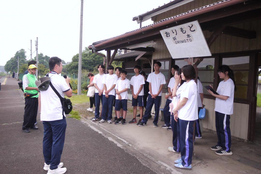 市職員やちくせい観光ボランティアガイドから折本駅の説明を聞く生徒たち=筑西市折本
