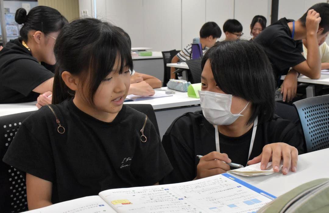 夏休みの宿題に苦戦する小学生を手助けする高校生ボランティア(右)=水戸市役所