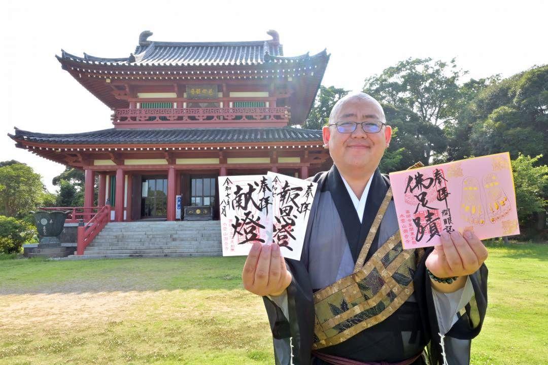 仏足石開眼記念(右)と万燈会限定の御朱印を持つ村上定運住職。後方は潮音寺本堂=潮来市日の出
