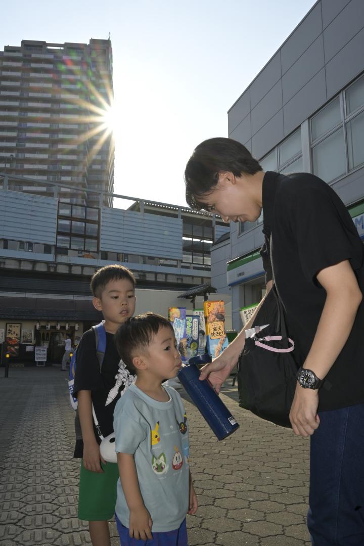 古河駅前でバス待ちをしながら、水分補給する子どもたち=5日午後、古河市東