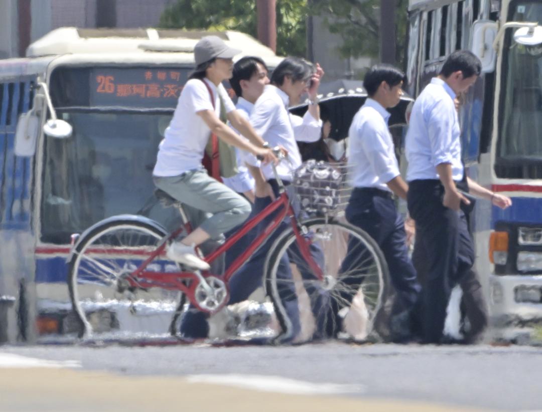 猛暑の中を暑そうに行き交う人たち。かげろうの影響で自転車の車輪がぐにゃりとゆがんで見える=5日午後0時13分、水戸市南町