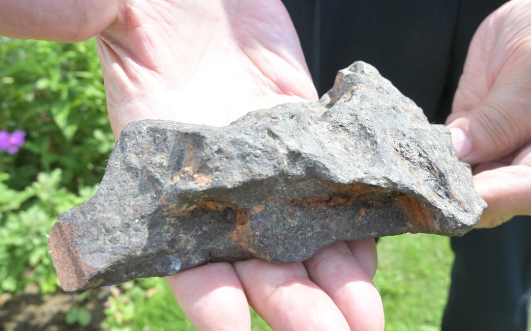 大きな穴が開いた畑の跡地で、1967年に見つかった砲弾の破片とみられる金属の塊。鋭利な断面や見た目に反した重さがある=水戸市吉沼町

