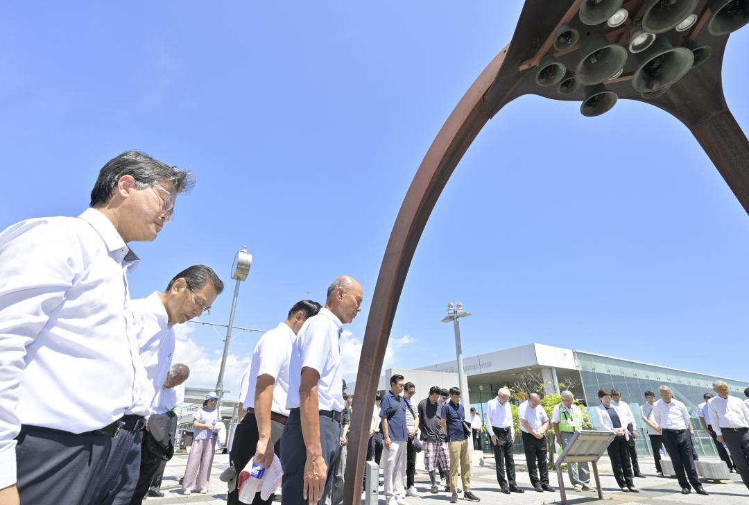 「平和の鐘」の前で黙とうする参加者=15日正午、日立市幸町