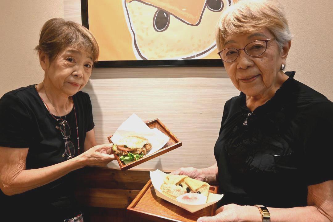 とりでバーガーを手にする雨宮由利子さん(左)と市の鳥「フクロウ」をイメージした、いなりずしを持つ姉・田中亜子さん=取手市新町
