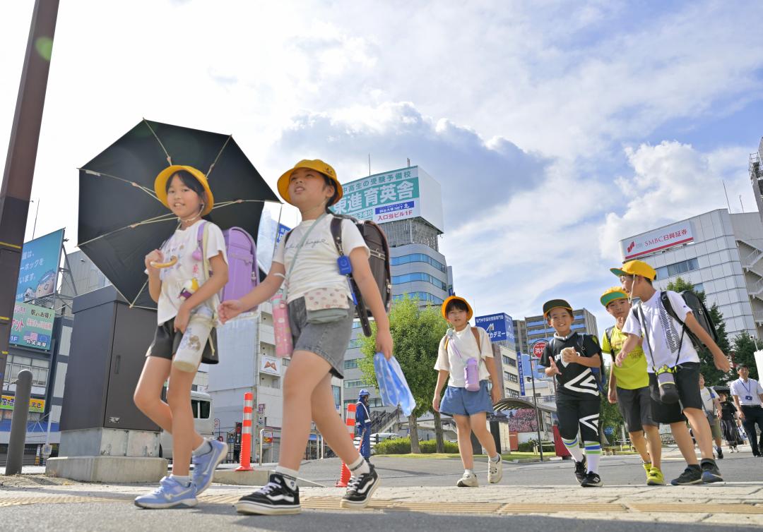 強い日差しが降り注ぐ中、日傘を差したり水筒を肩から掛けたりして下校する児童ら=2日午後2時41分、水戸市三の丸