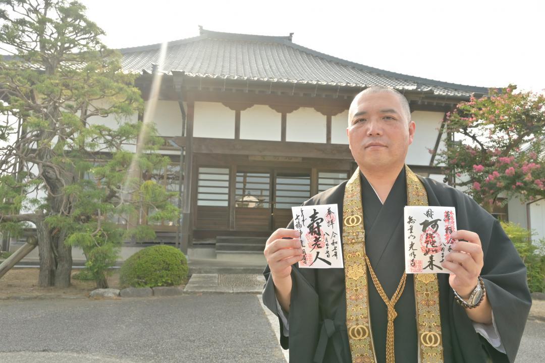 光明寺本堂の前で御朱印を手に立つ倉持武士住職=取手市桑原

