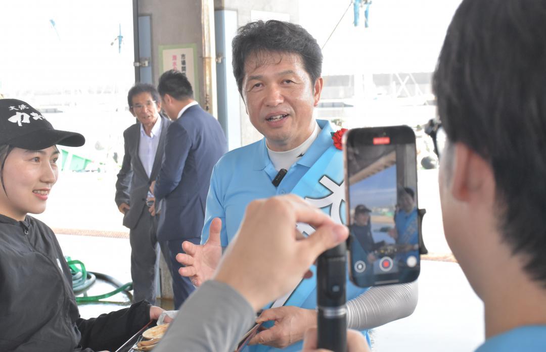 遊説先で交流サイト(SNS)への投稿用動画を撮影する大井川和彦氏=8月21日午後、大洗町磯浜町

