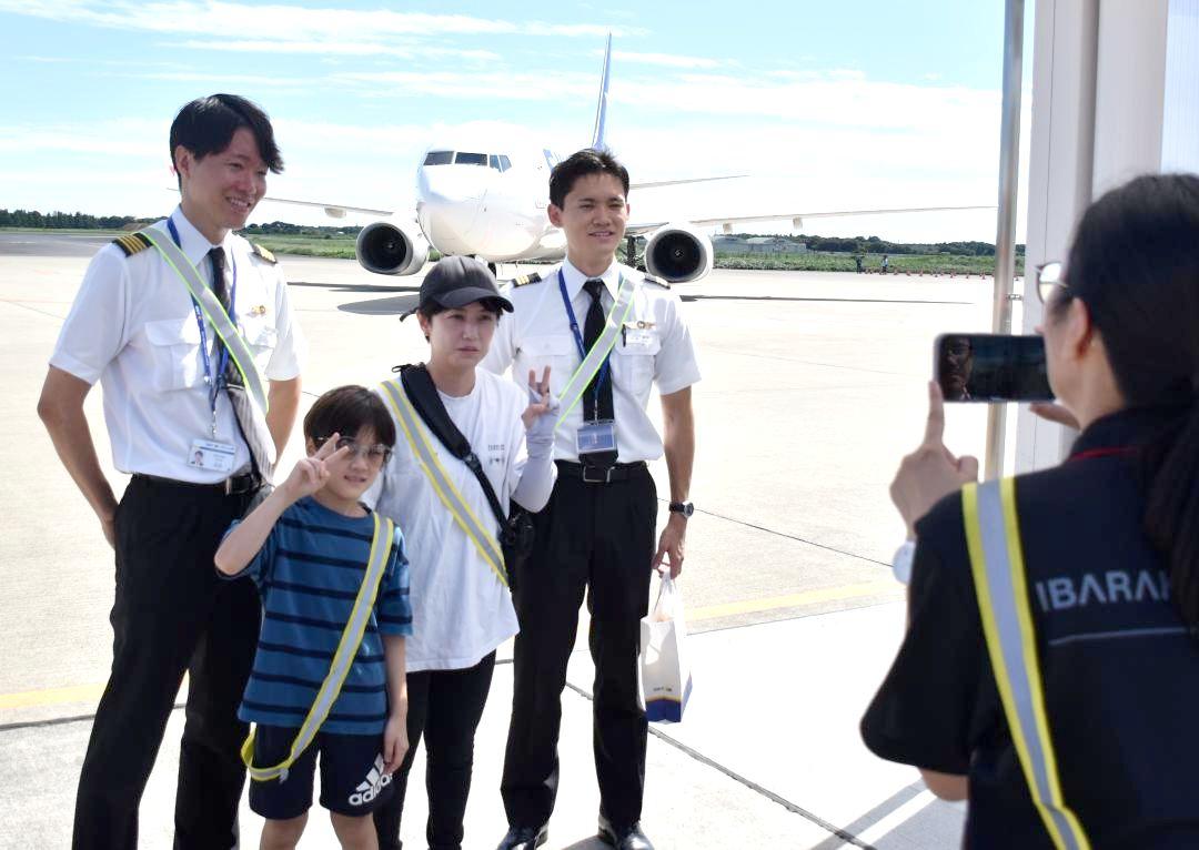 旅客機を背景にスカイマークの現役パイロットと記念撮影する参加者=小美玉市与沢

