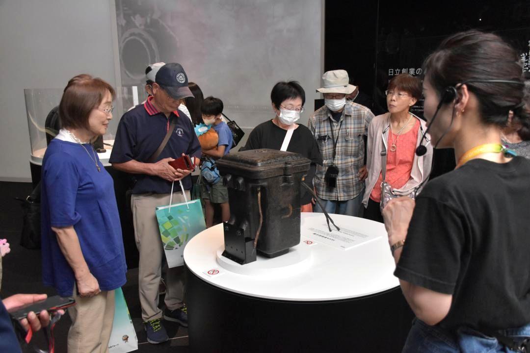 日立オリジンパークで解説者(右)の案内で展示物を見る来館者=日立市大みか町