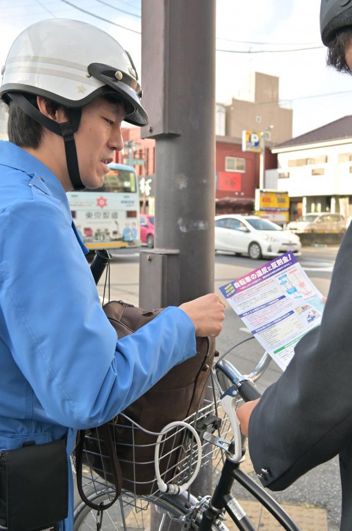 街頭指導で自転車利用者に改正道交法などを説明する警察官(左)=10月31日、土浦市大和町