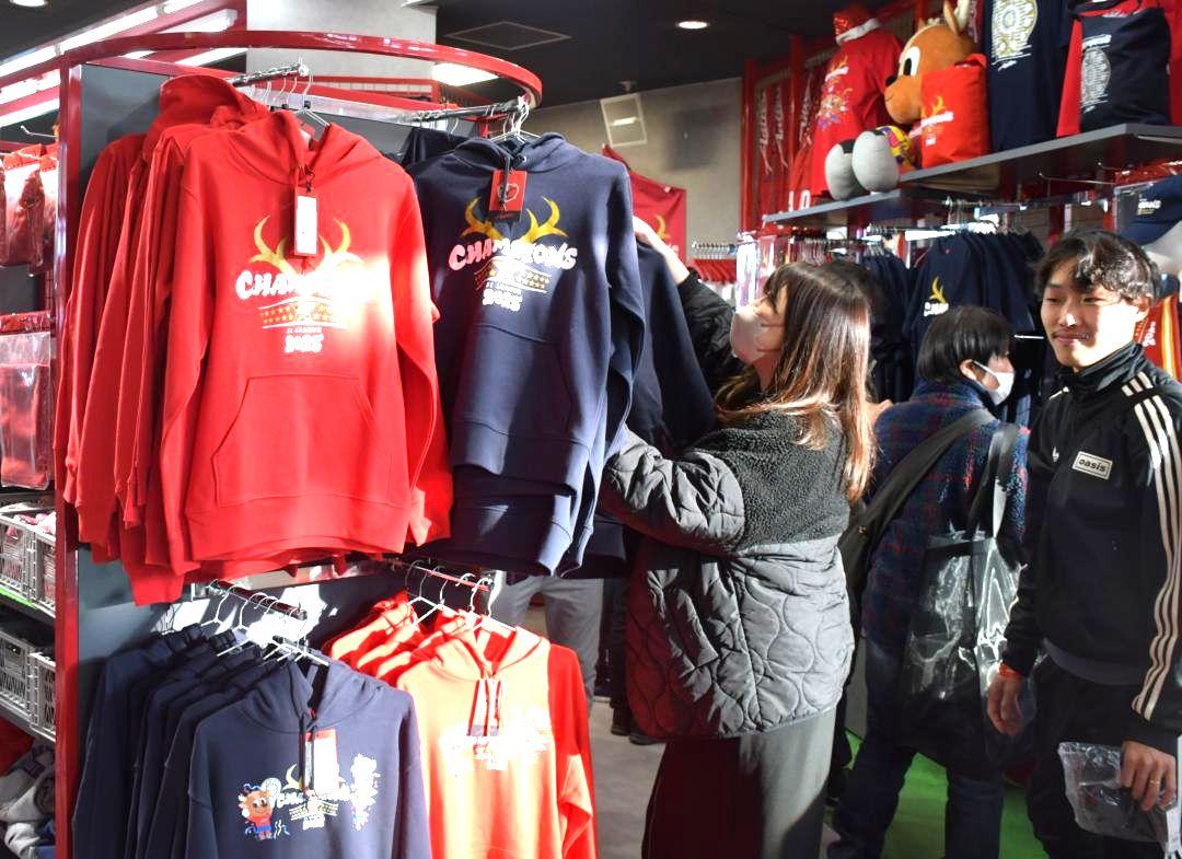 J1鹿島アントラーズのクラブハウス内店舗に並んだ優勝記念グッズを手にする多くのサポーターら=鹿嶋市粟生