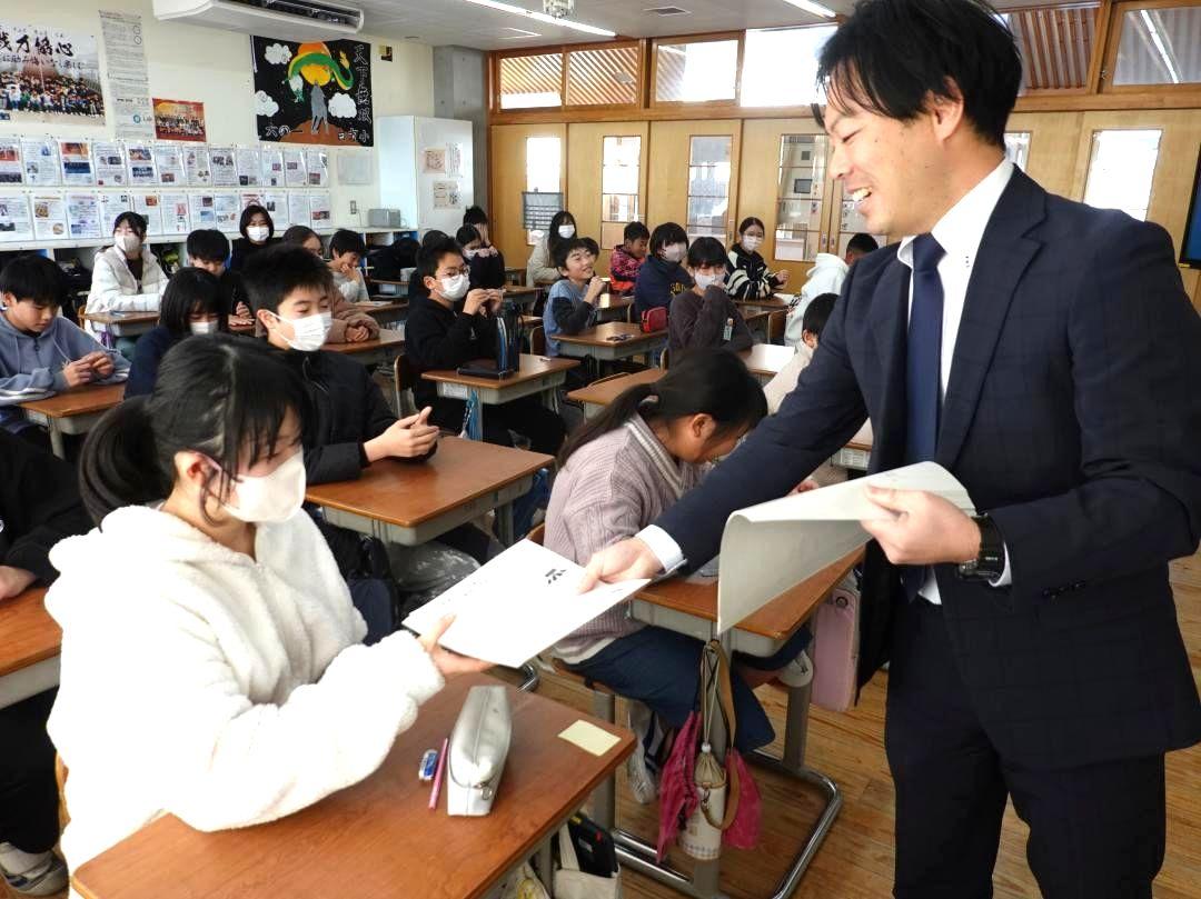 6年生クラスの児童に抱負を書く用紙を配る担任教諭(右)=東海村白方