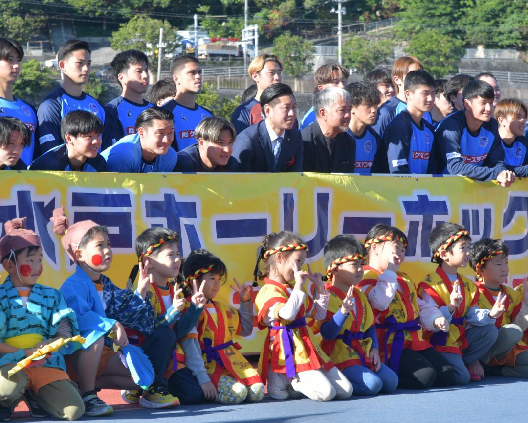 歓迎セレモニーを行ったJ1水戸の選手と豊見城市の徳元次人市長(中段右から6人目)。下段は地元保育園の園児たち=豊見城総合公園陸上競技場