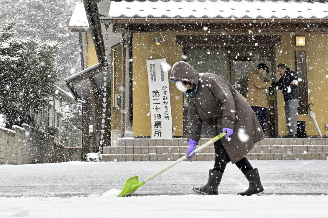 雪が降る中、投票所の前を雪かきする女性=8日午前7時48分、かすみがうら市深谷