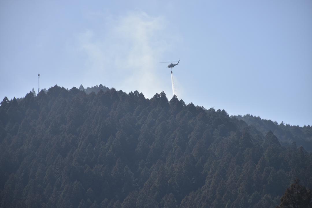 白煙に放水する自衛隊の中型ヘリ=22日午前10時40分ごろ、常陸太田市折橋町